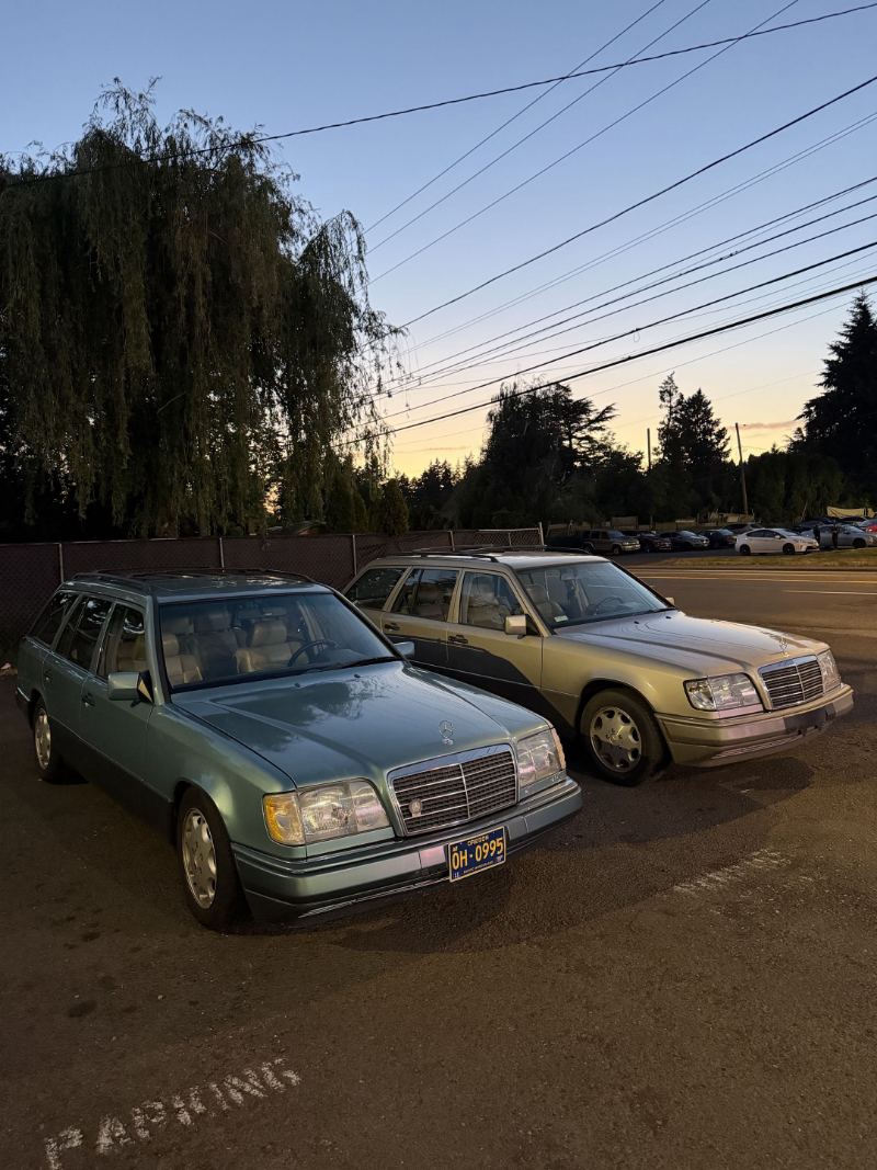 Two Mercedes-Benz W124 E-Class wagons parked outside Trafton's Foreign Auto at dusk